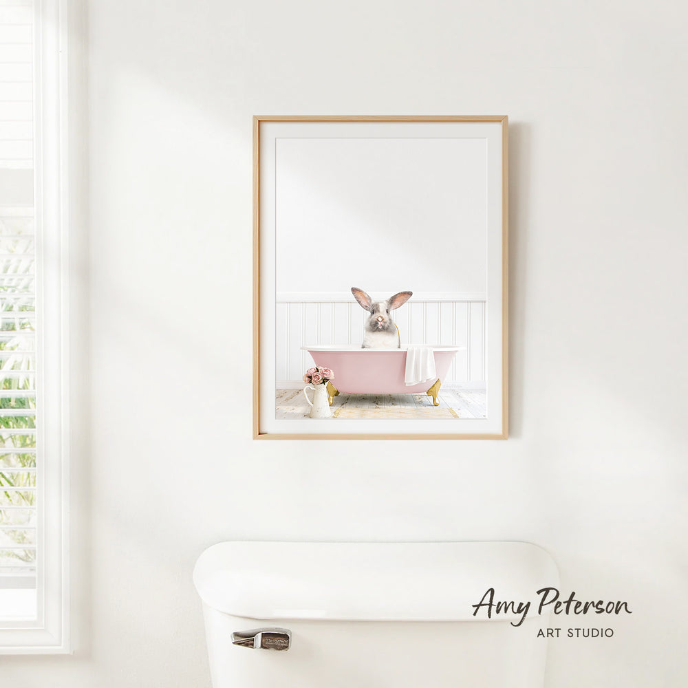 A framed image of a rabbit sitting in a pink bathtub, with a window and toilet visible in the background.