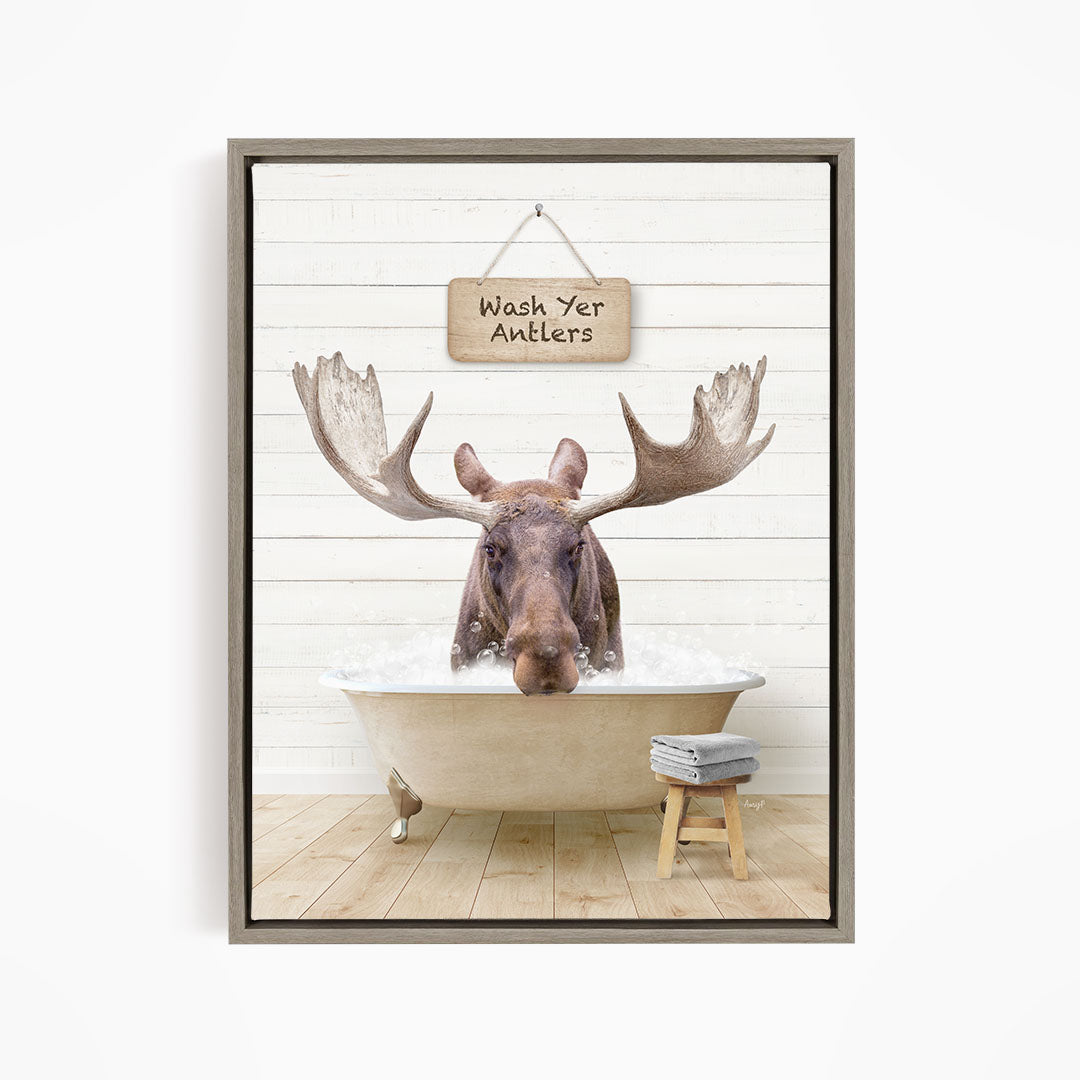A moose is sitting in a bathtub filled with water, with a sign above it that says "Wash Yer Antlers".