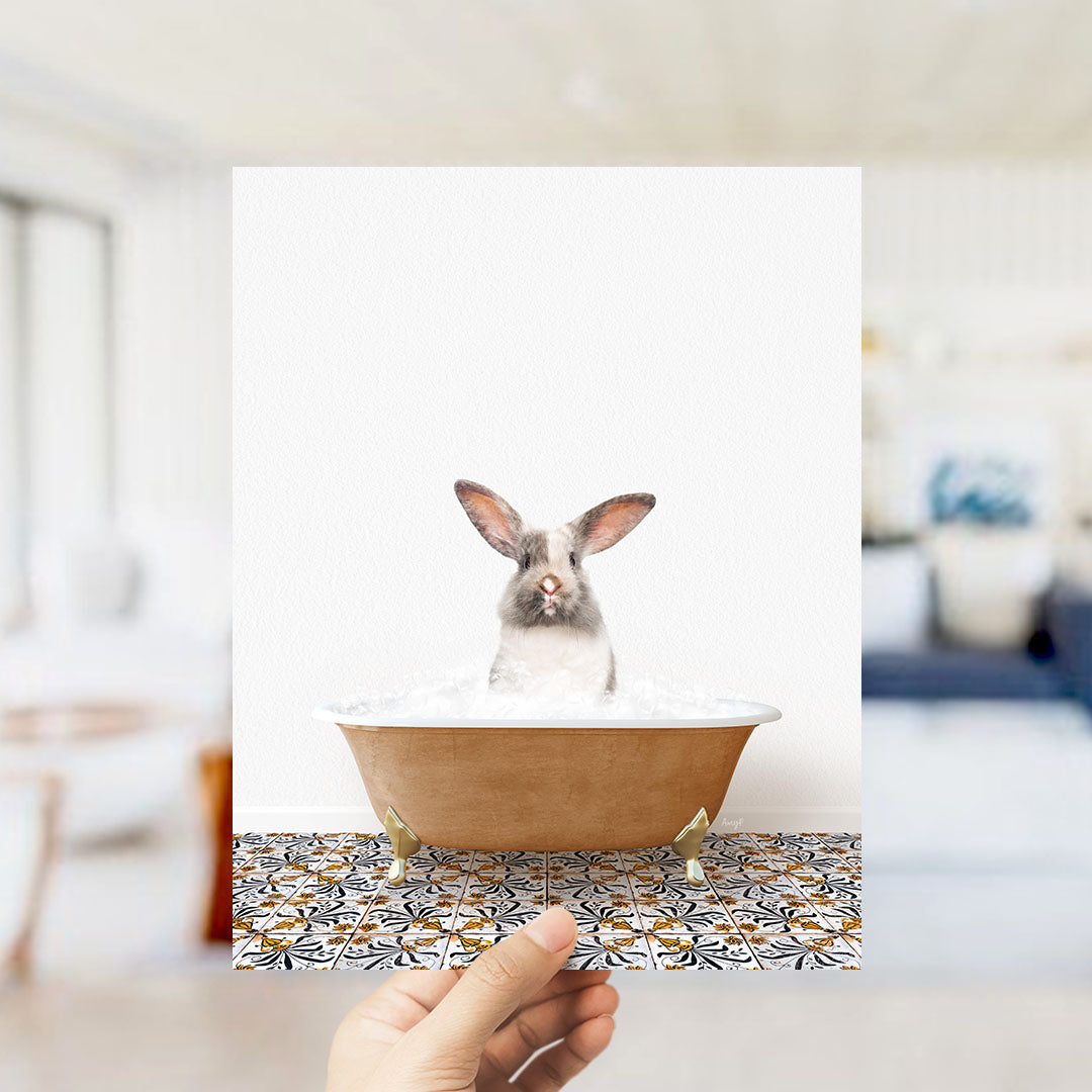 A hand holds up a framed image of a rabbit sitting in a bathtub filled with bubbles, with a patterned tile floor visible in the background.