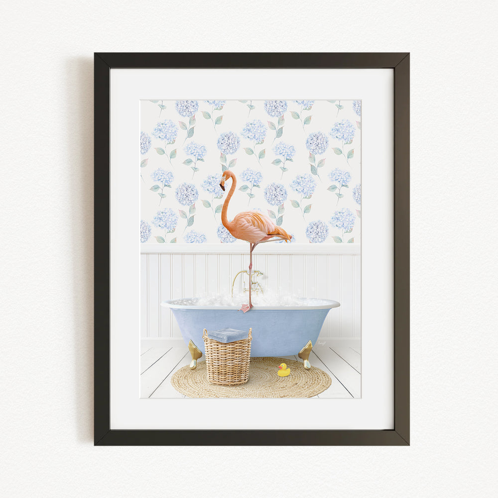 A framed image depicting a pink flamingo standing on a blue bathtub, with a blue and white floral pattern on the wall behind it.