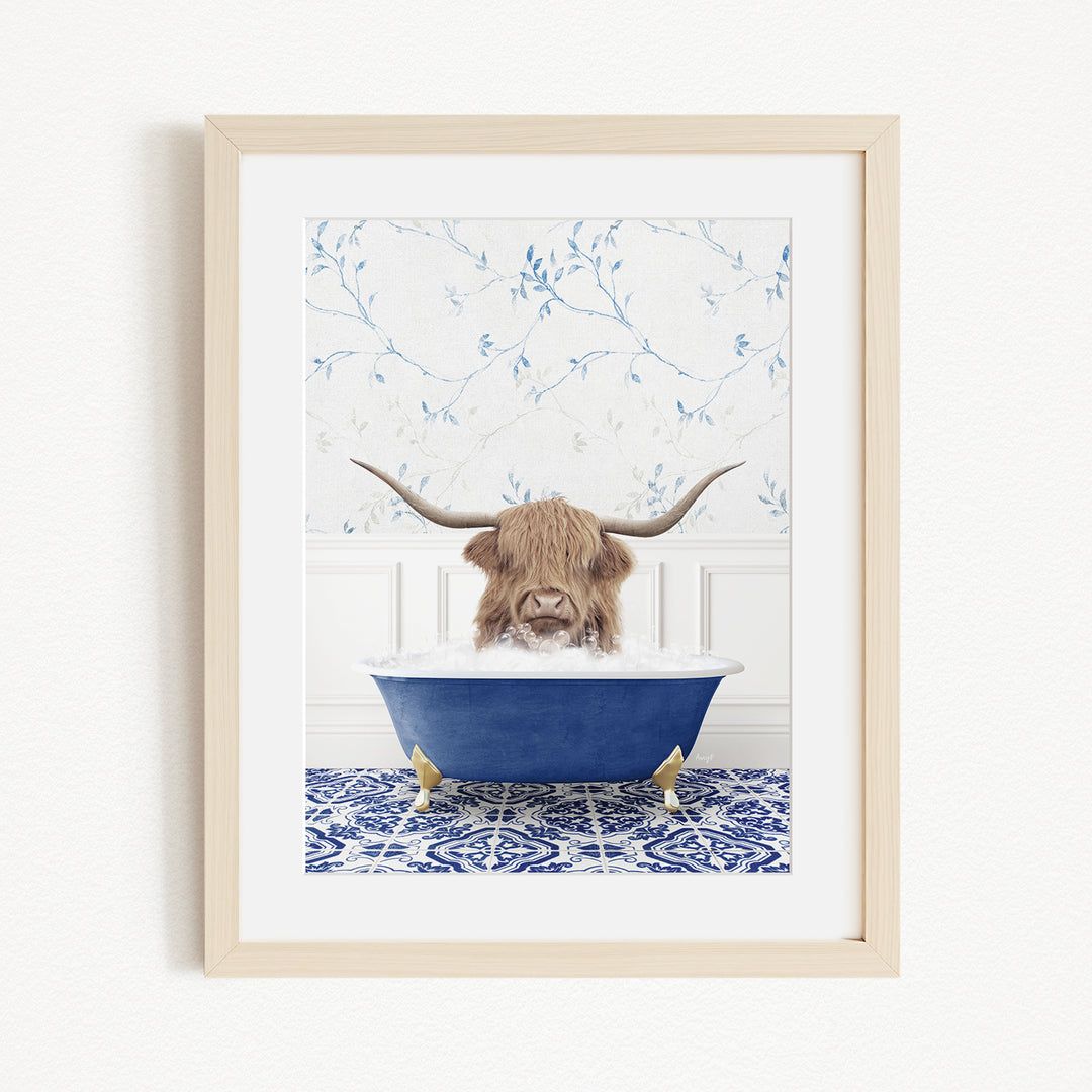 A framed image depicting a Highland cow with long horns sitting in a blue bathtub, surrounded by a blue and white floral patterned wall.