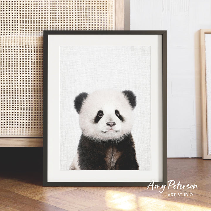 A framed photograph of a panda bear is displayed on a wooden floor, with a beige woven basket visible in the background.
