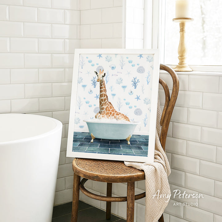 A framed painting of a giraffe sitting in a bathtub is displayed on a wooden chair in a bathroom setting.