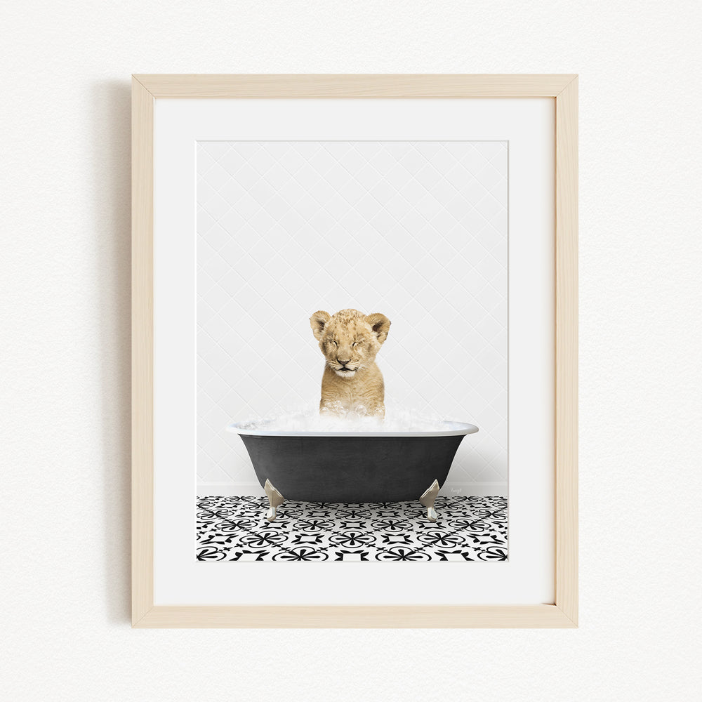 A young lion cub sitting in a black bathtub filled with water, surrounded by a black and white patterned floor.
