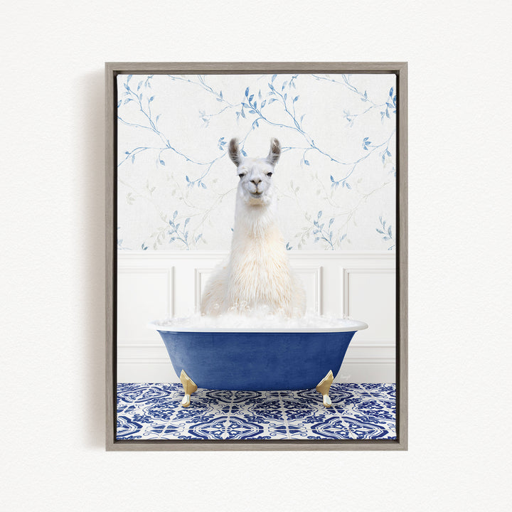A white llama sitting in a blue bathtub filled with bubbles, surrounded by a blue and white patterned rug and a floral wallpaper background.