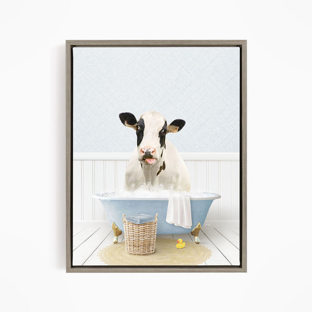 A black and white cow is sitting in a blue bathtub filled with water, surrounded by a basket of rubber ducks and a towel.