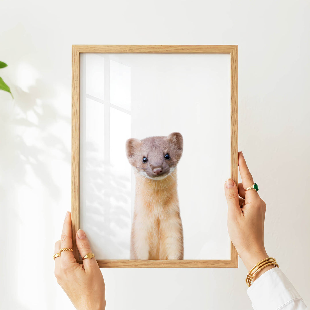 A person's hands are holding a wooden frame with a picture of a small, furry animal inside it.