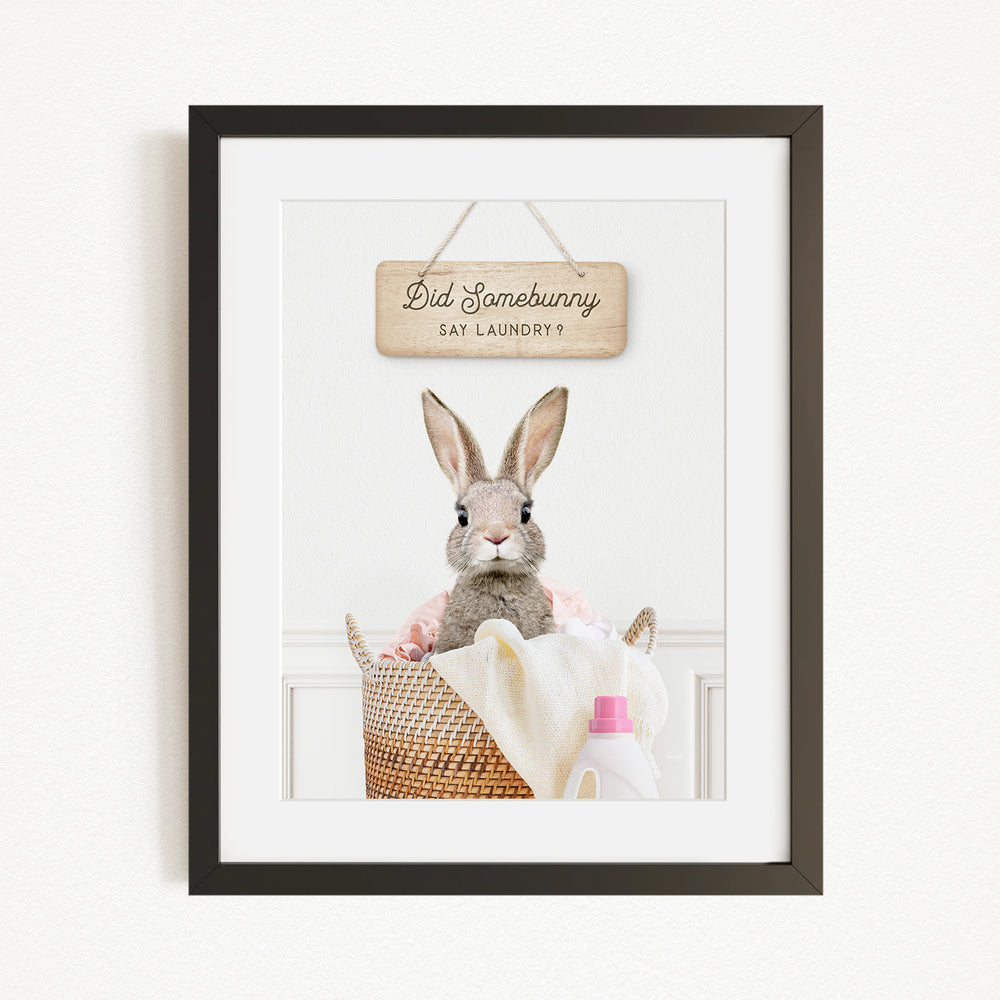 A framed image of a rabbit sitting in a basket filled with laundry, with a sign above that says "Did Somebunny Say Laundry".
