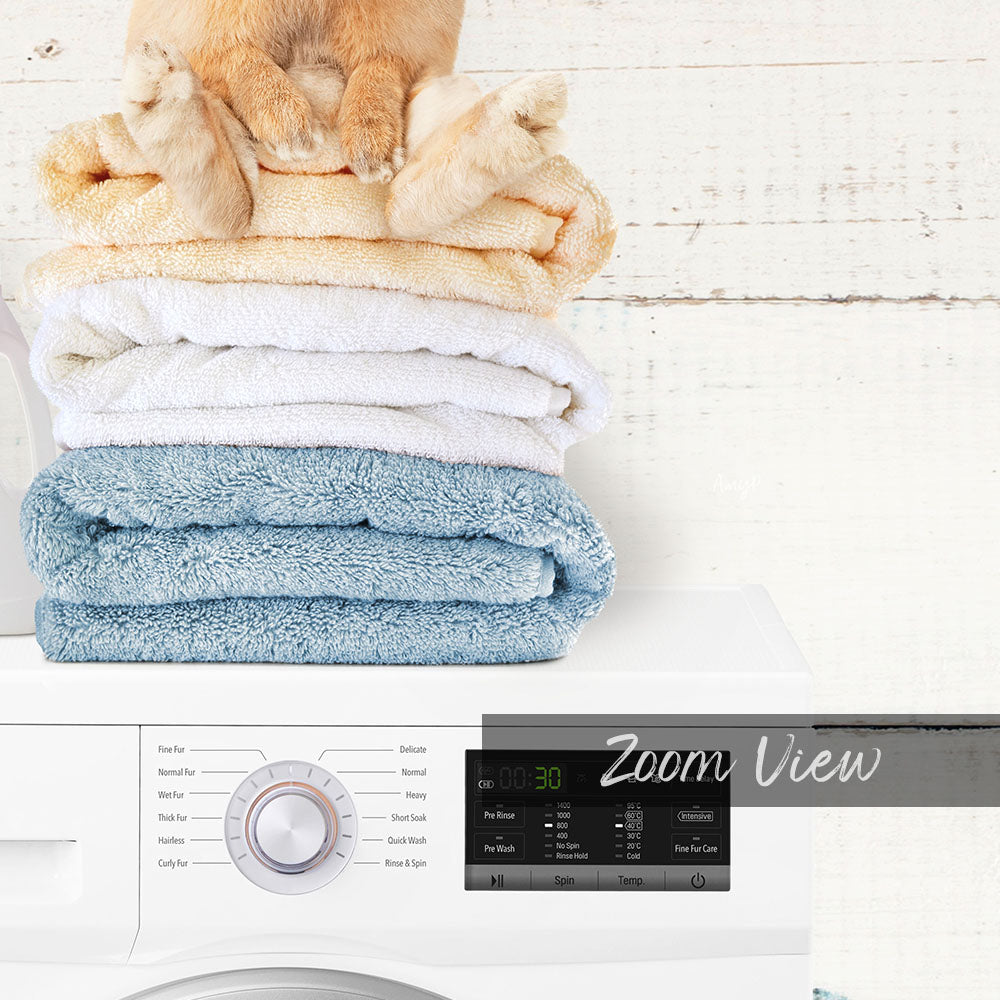 A stack of folded towels on top of a washing machine, with a digital display and control panel visible below.