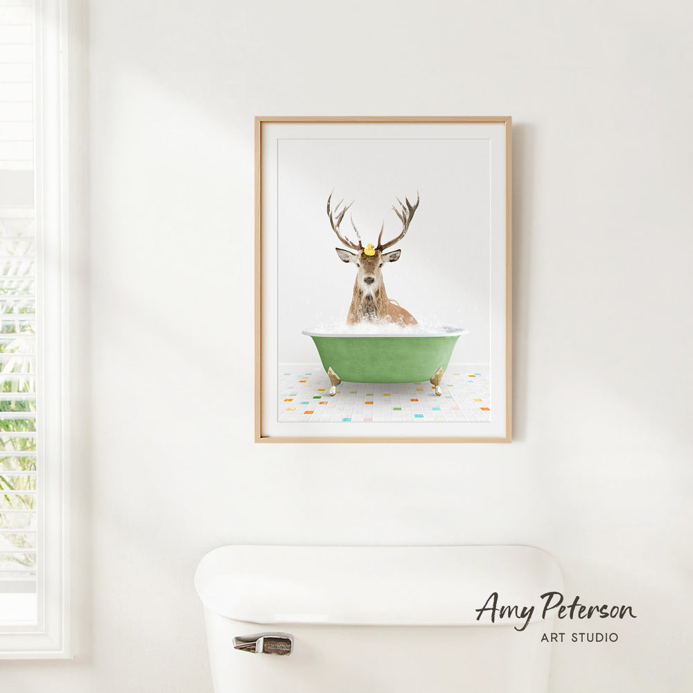 A framed image of a deer sitting in a green bathtub, with a white toilet in the foreground.