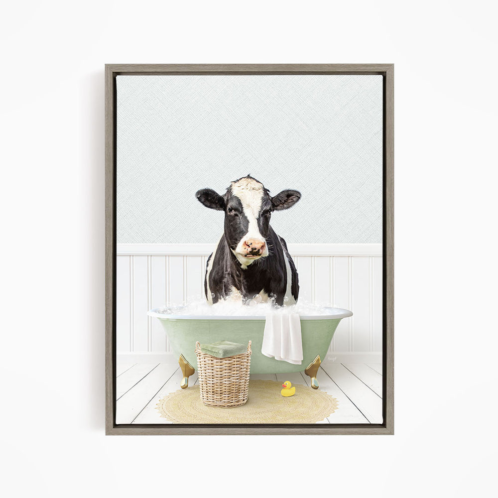 A black and white cow is sitting in a green bathtub filled with water, surrounded by a basket of toys and a yellow rubber duck.