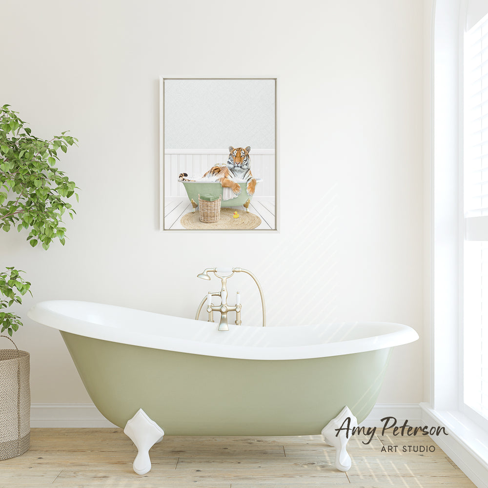 A framed image of a tiger sitting in a bathtub is displayed on the wall above a green clawfoot bathtub in a bright, white-walled bathroom.