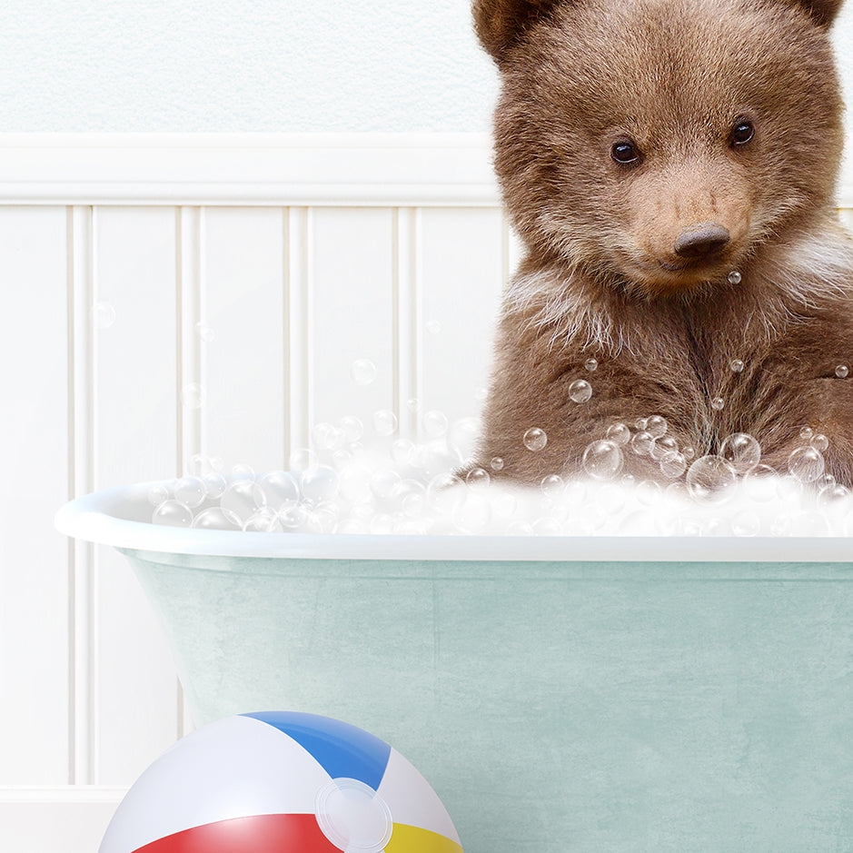 a brown bear sitting in a bath tub next to a beach ball