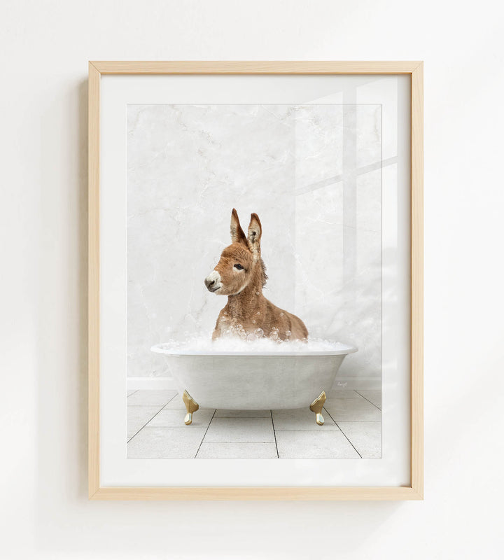 A donkey is sitting in a white bathtub filled with bubbles, looking directly at the camera.