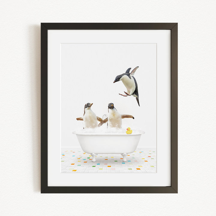 A framed image depicting two penguins sitting in a bathtub, with one penguin jumping out of the tub and another penguin sitting in the tub.