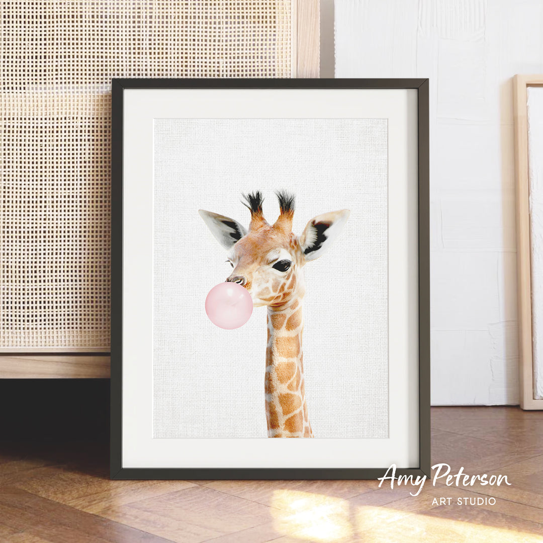 A framed print of a giraffe blowing a bubble with a pink bubble gum bubble.