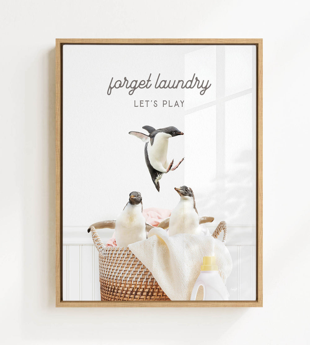 A framed image depicting three penguins in a basket, with the text "Forget laundry, let's play" written above them.