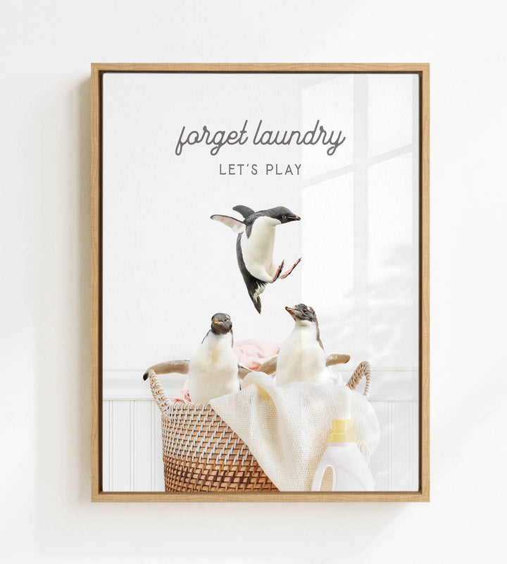 A framed image depicting three penguins in a basket, with the text "Forget laundry, let's play" written above them.
