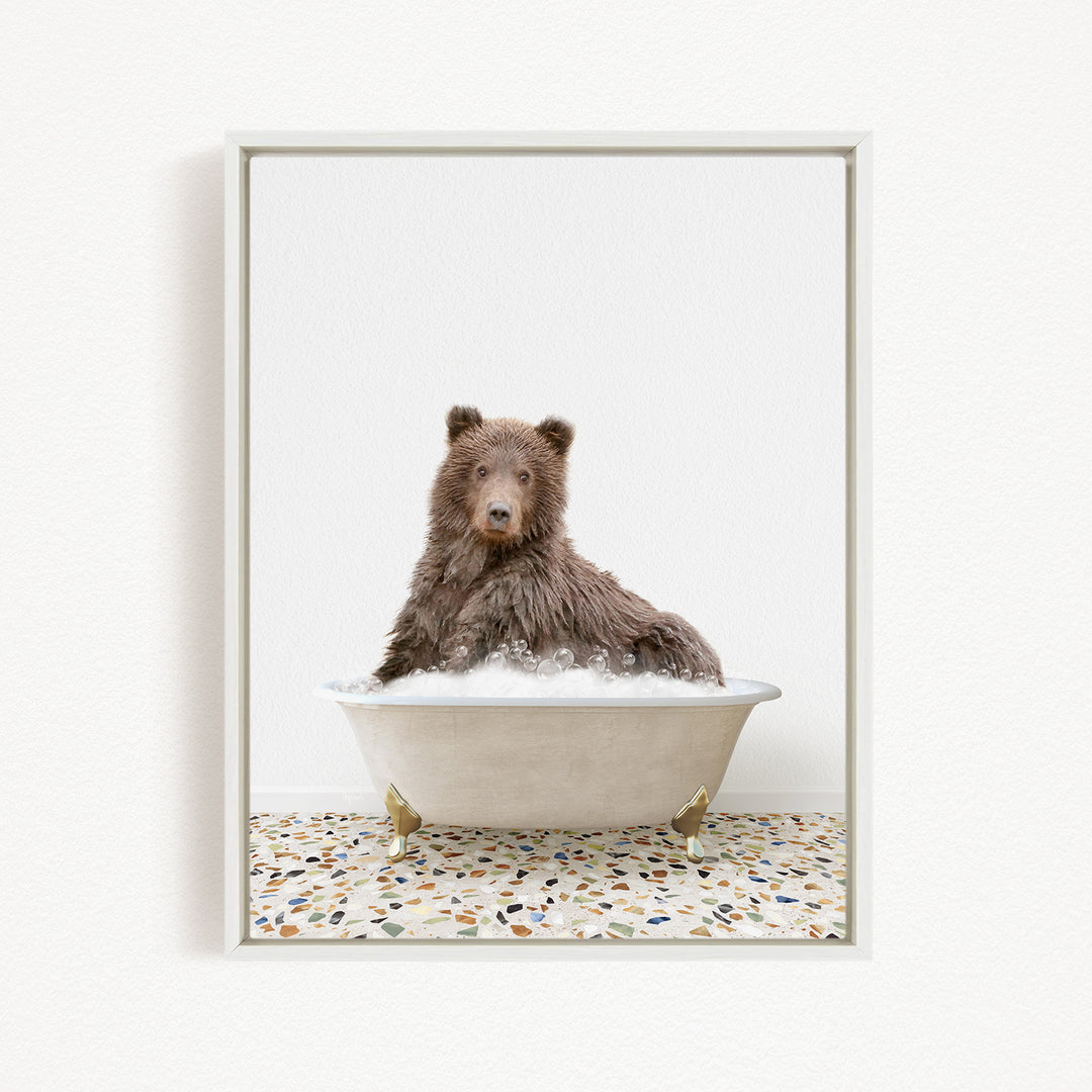 A brown bear sitting in a white bathtub filled with bubbles, looking directly at the camera.