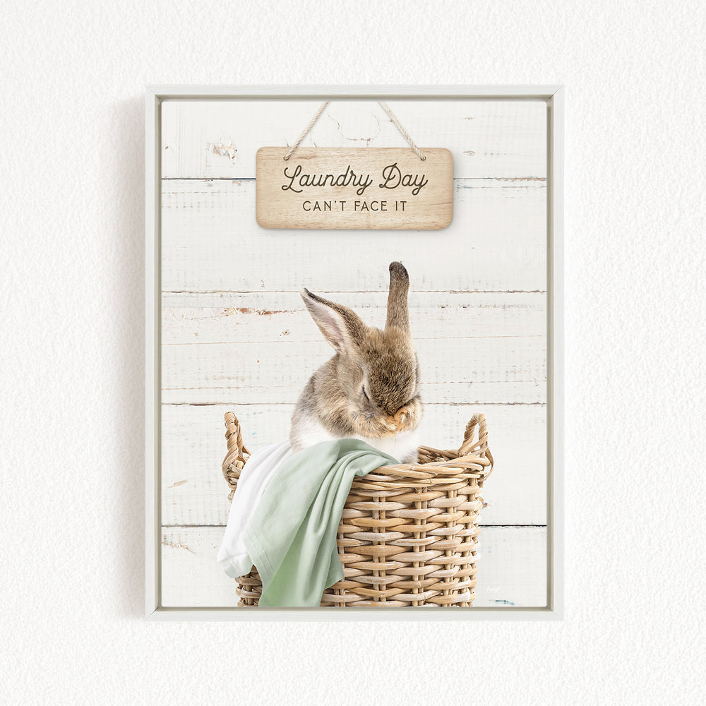 A cute rabbit sitting in a wicker basket, with a wooden sign above that says "Laundry Day Can't Face It".
