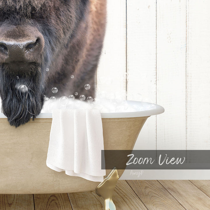 A close-up of a bison's head in a bathtub filled with bubbles, with a towel and wooden floor visible in the background.