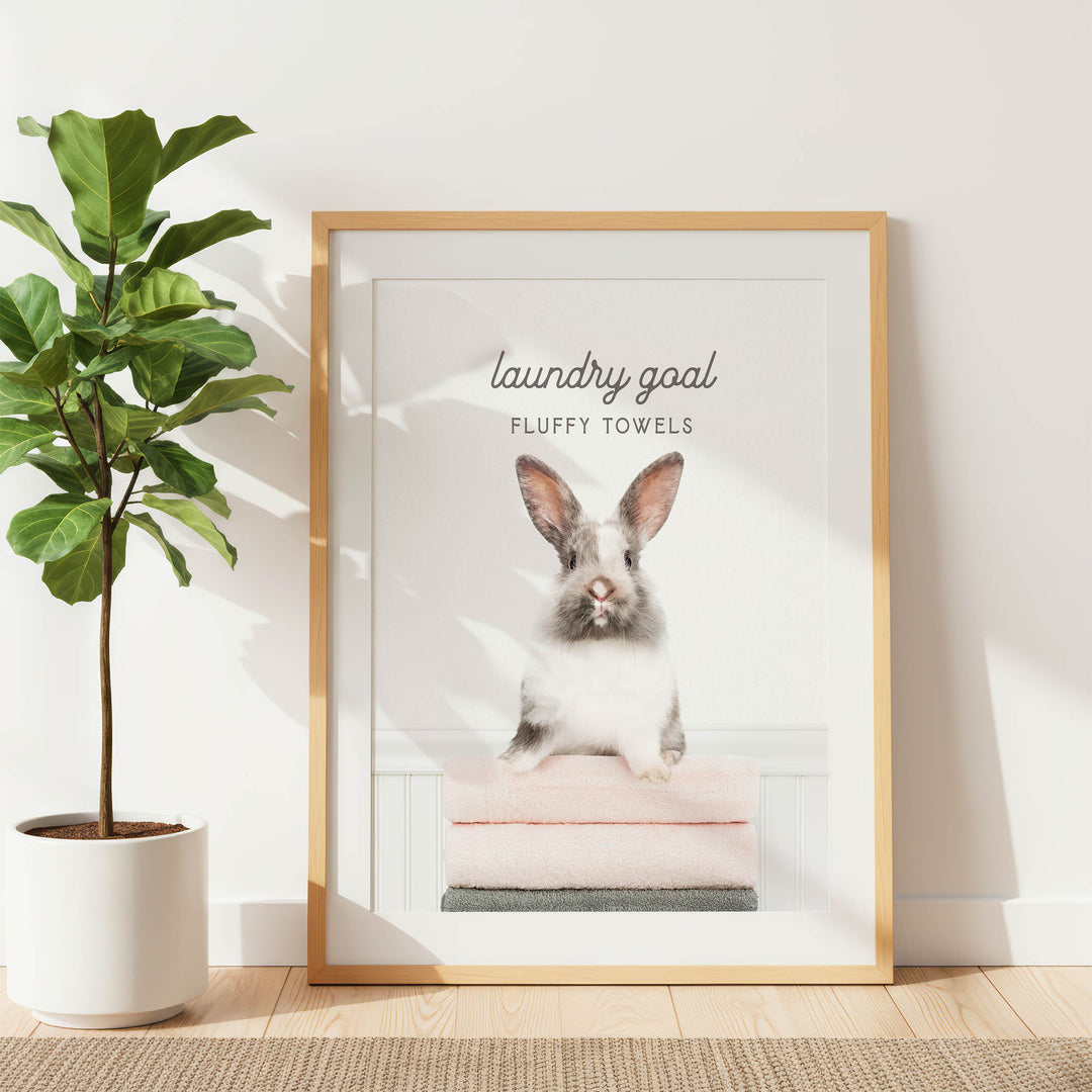 A framed poster with a picture of a rabbit sitting on a stack of fluffy towels, accompanied by the text "laundry goal FLUFFY TOWELS".