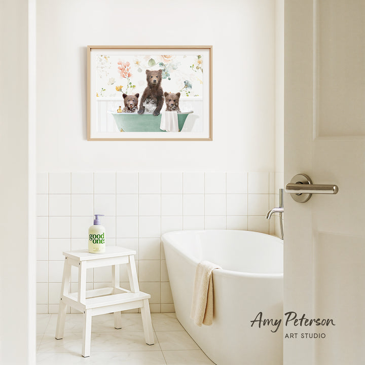 A framed image of three bears sitting in a bathtub is hanging on the wall above a white bathtub in a bathroom.