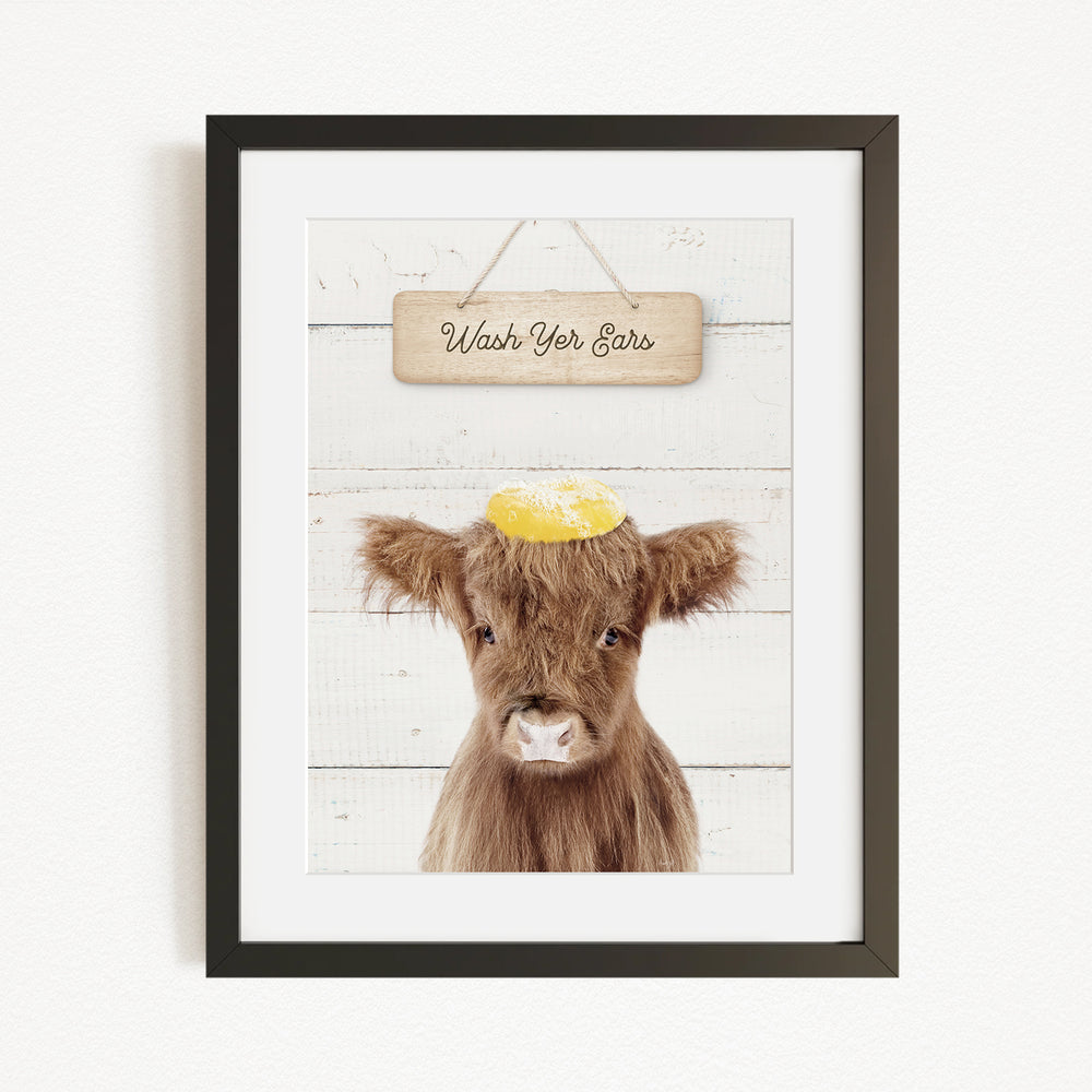 A framed image of a brown cow with a yellow ear tag, accompanied by a wooden sign that reads "Wash Your Ears".