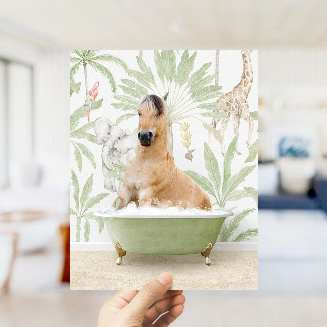 A hand holds up a framed image depicting a horse sitting in a bathtub surrounded by tropical foliage, including a giraffe and palm trees.