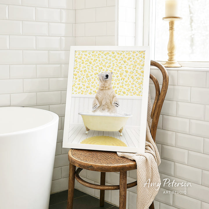 A framed image of a polar bear sitting in a bathtub, surrounded by yellow flowers, is displayed on a wooden chair in a bathroom setting.