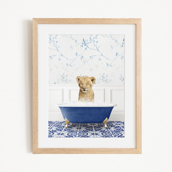 A young lion cub sitting in a blue bathtub filled with water, surrounded by a blue and white patterned rug.