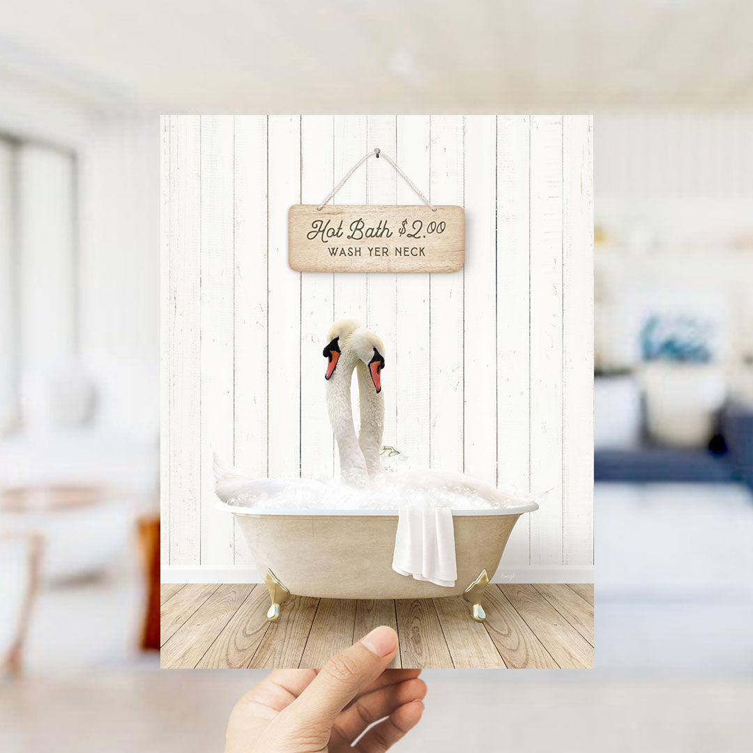 A hand holding a framed image of two swans sitting in a bathtub, with a sign above them advertising a hot bath for $2.00.