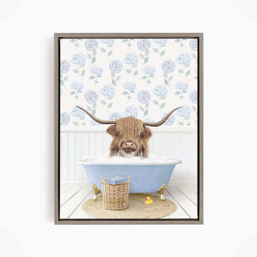 A brown cow with long horns is sitting in a blue bathtub filled with water, surrounded by a wicker basket and yellow rubber ducks.