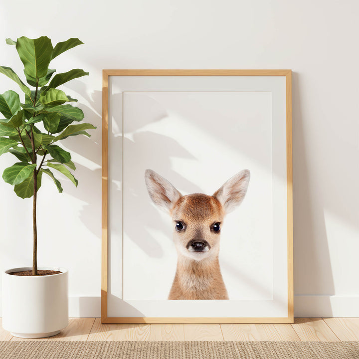 a framed photograph of a deer with large ears, positioned on a wooden floor next to a potted plant.