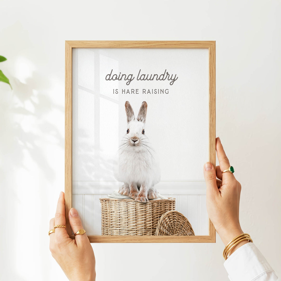 A person's hands are holding a picture frame with a photo of a white rabbit sitting in a wicker basket.