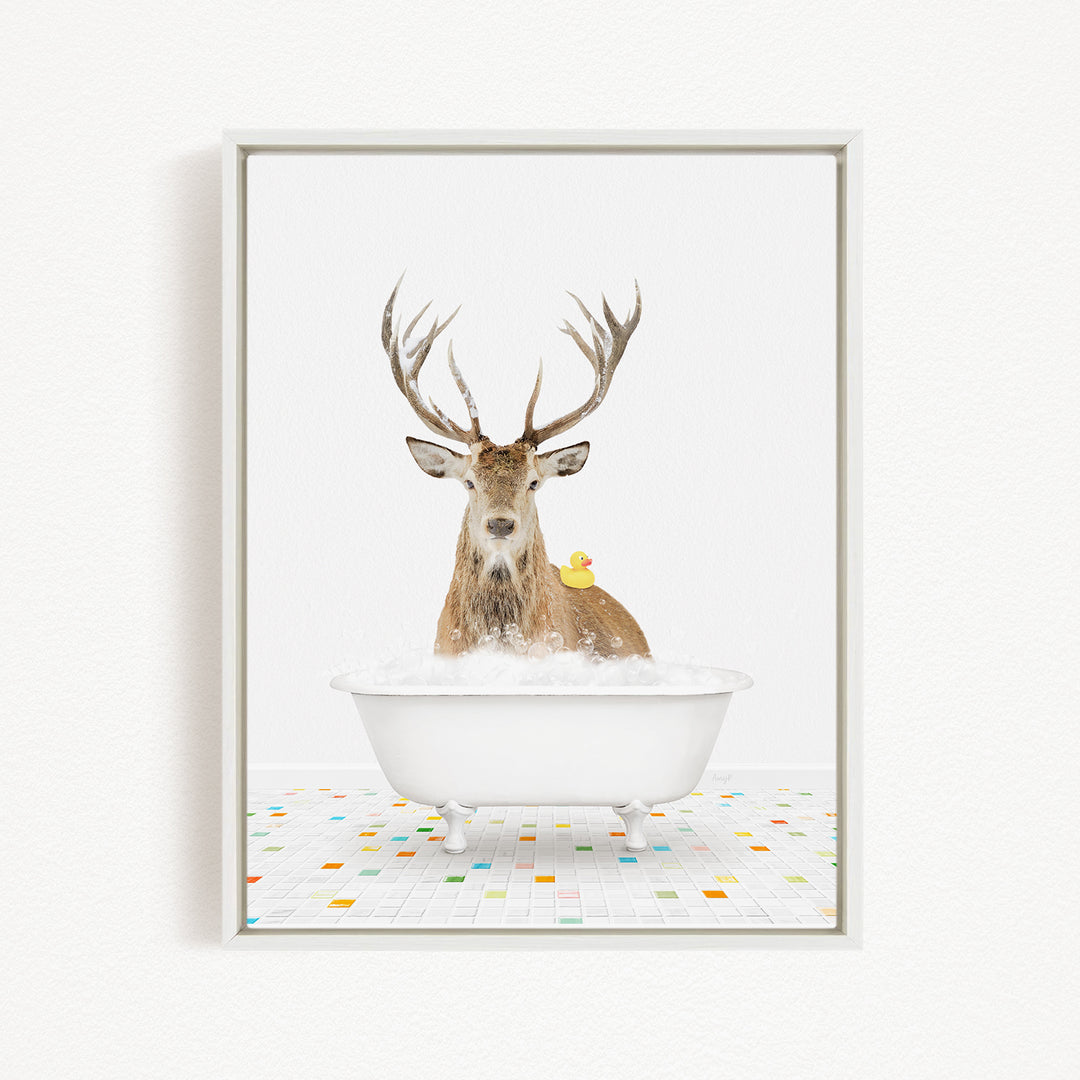 A deer with large antlers is sitting in a white bathtub filled with bubbles, with a yellow rubber duck resting on its back.