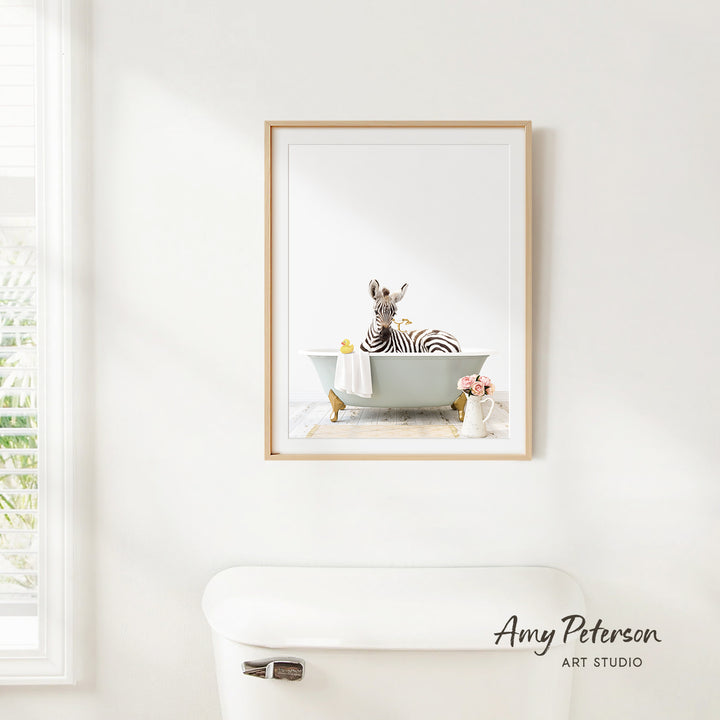 A framed image of a zebra sitting in a bathtub, surrounded by various bathroom items such as a vase and a towel.