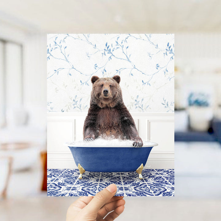 A brown bear sitting in a blue bathtub filled with water, surrounded by a blue and white floral patterned wall.