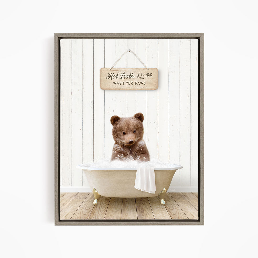 A brown bear sitting in a white bathtub, with a wooden sign above it that reads "Hot Bath $2.00 WASH YOUR Paws".