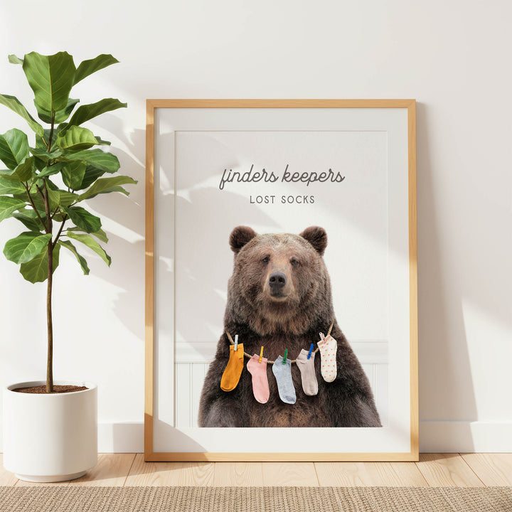 A framed poster featuring a large brown bear wearing a variety of colorful socks, with the text "finders keepers" and "lost socks" written above the bear.