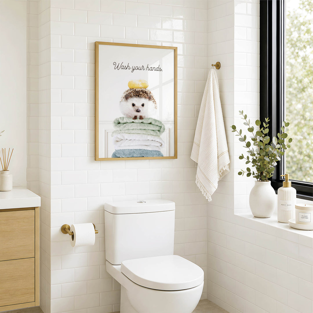 A bathroom with a white toilet, a framed poster of a hedgehog, and a window with greenery.