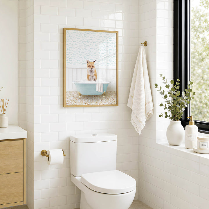 A bathroom with a white toilet, a framed picture of a cat sitting in a bathtub, and a window with greenery on the sill.