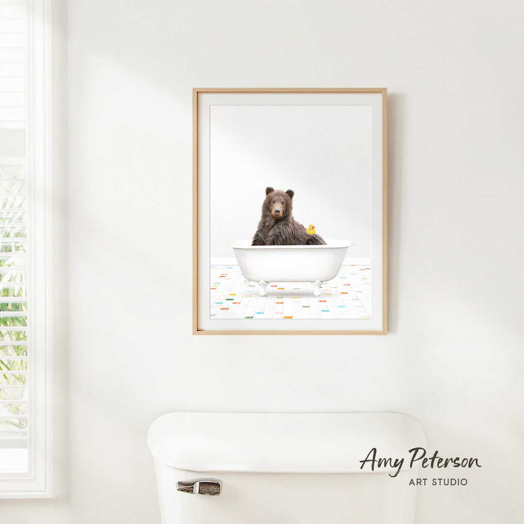 A framed image of a brown bear sitting in a white bathtub, surrounded by colorful tiles on the floor.