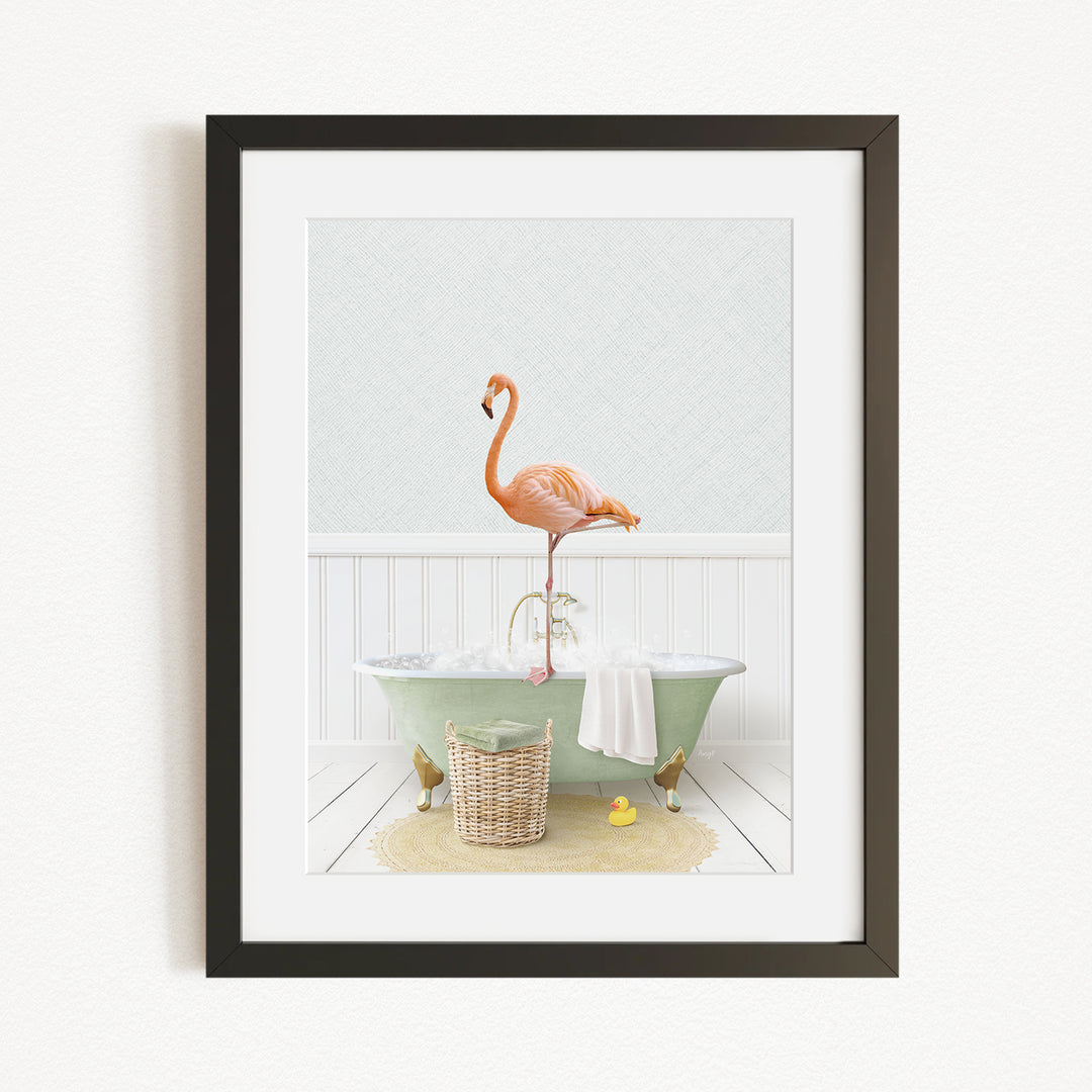 A framed image depicting a pink flamingo standing on the edge of a green bathtub, with a basket of bath toys and a yellow rubber duck nearby.