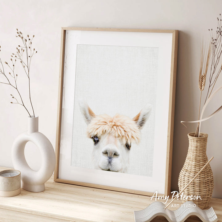 a framed picture of a llama with a fluffy white mane, placed on a wooden surface next to two decorative vases.