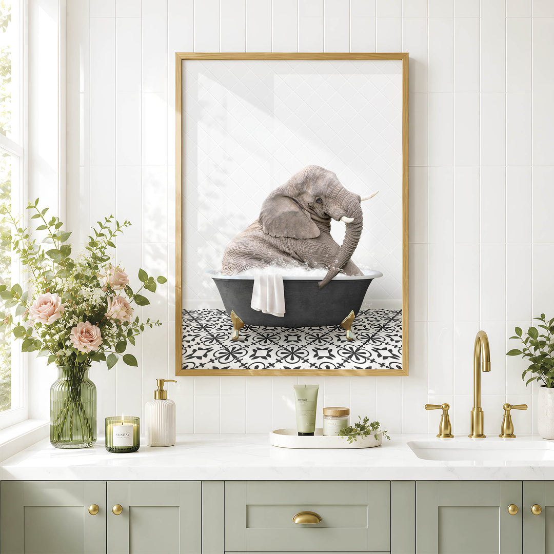 A framed image of an elephant sitting in a bathtub, surrounded by flowers and a decorative vase, is displayed on a white tiled wall above a bathroom sink.