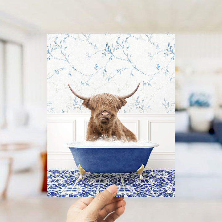 A brown cow with horns is sitting in a blue bathtub filled with water, surrounded by a blue and white floral patterned wall.