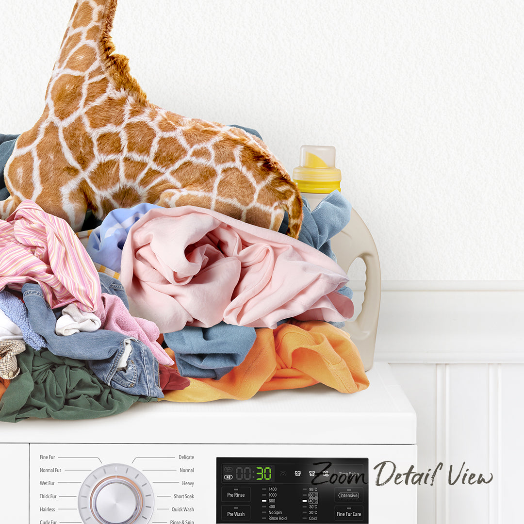 A laundry basket filled with various clothes, including a stuffed giraffe, sits on top of a washing machine.
