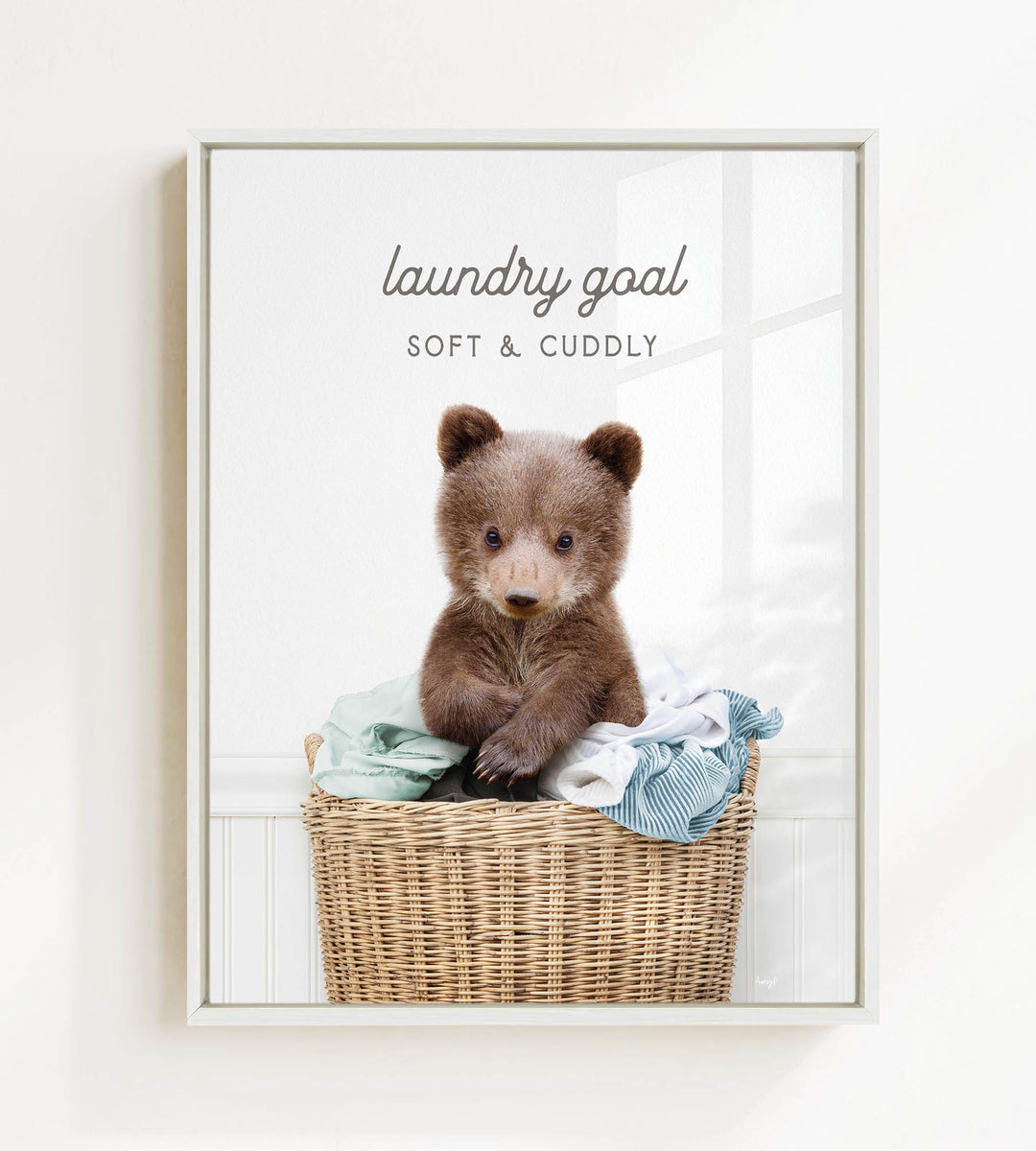 A cute brown bear sitting in a wicker laundry basket filled with clothes, with the text "laundry goal" and "soft & cuddly" written above it.
