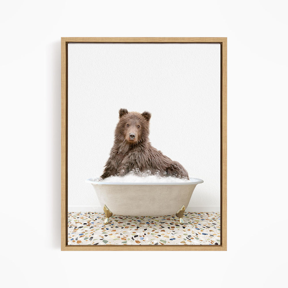 A brown bear sitting in a white bathtub filled with bubbles, looking directly at the camera.